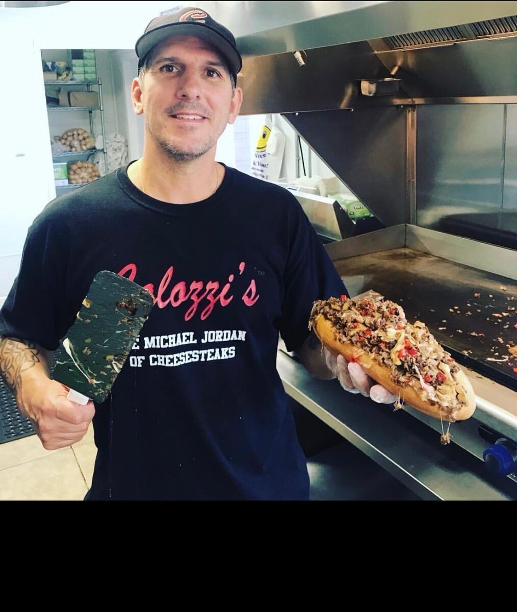 Al Calozzi at the griddle holding a loaded Calozzi's cheesesteak